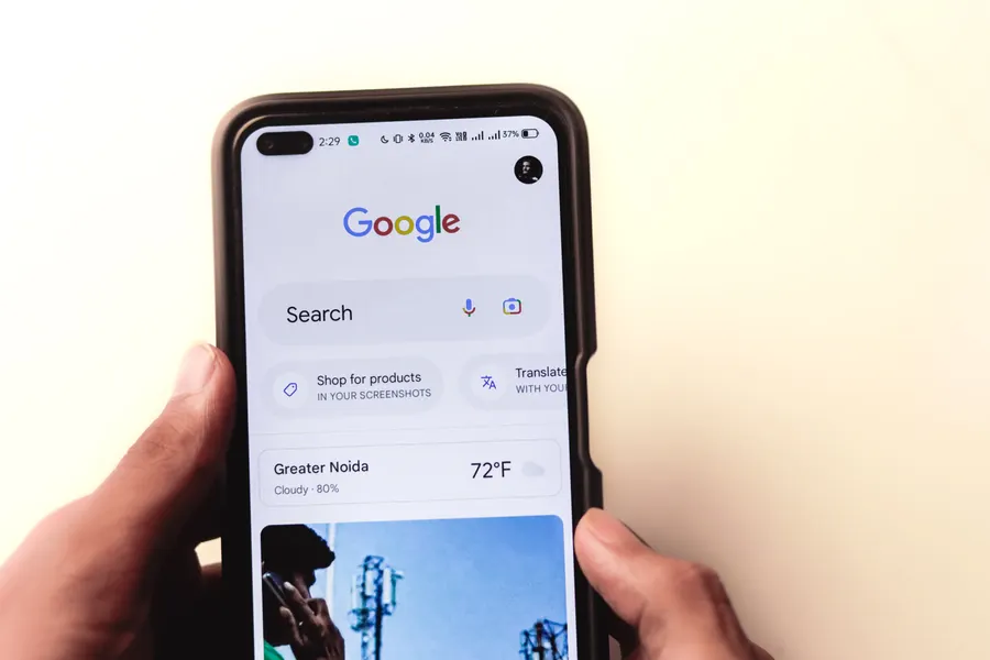 Mão segurando celular com busca no Google em destaque