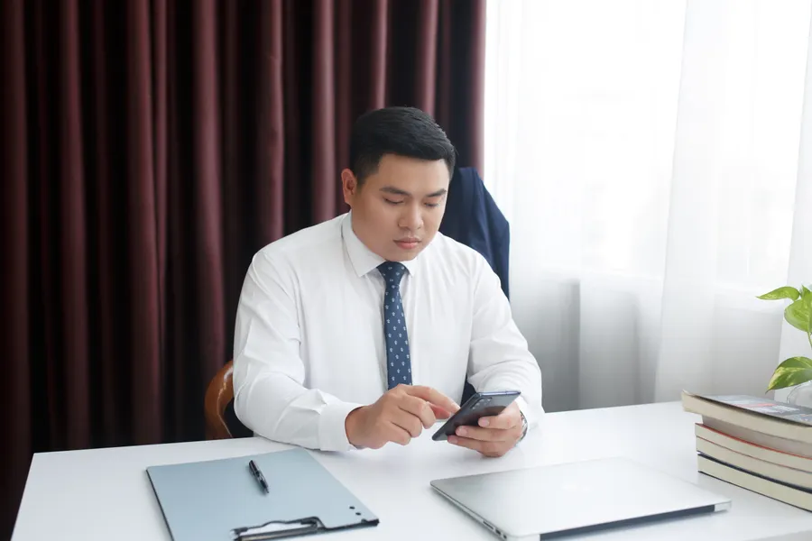 Advogado de terno consultando o celular na mesa do escritório