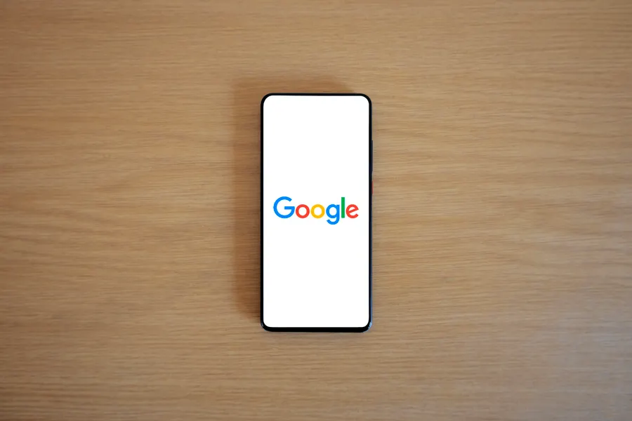 Celular exibindo a página de busca do Google sobre uma mesa de madeira