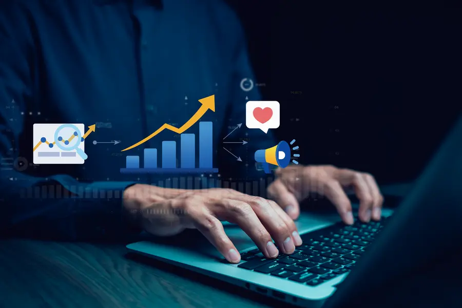 Mãos digitando em notebook com ícones de crescimento e engajamento