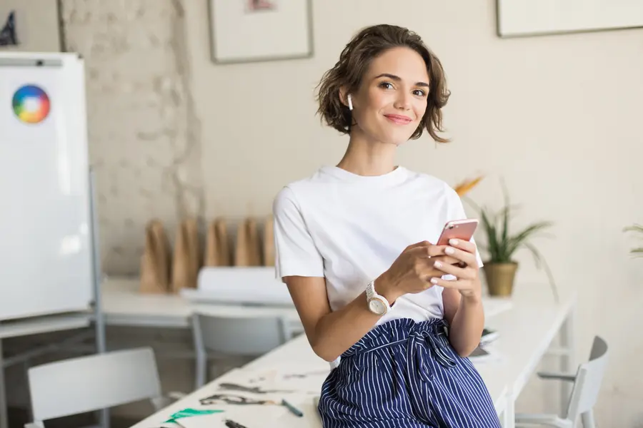 Mulher sorrindo enquanto usa o celular em ambiente de trabalho